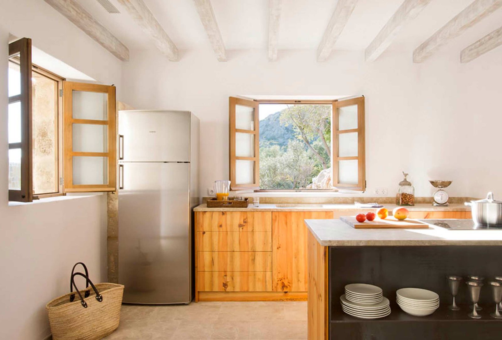 Cocina con muebles de madera, isla oscura, vigas blanqueadas y ventana abierta a la montaña