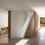 Pasillo con suelo de microcemento, escalera volada de roble y puertas correderas de madera