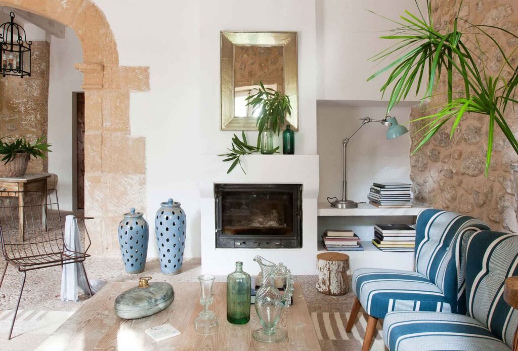 Rincón del salón con chimenea blanca, arco de piedra, sillones de rayas azules y jarrones calados