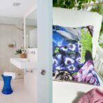 Baño de piedra beige con ducha de cristal y taburete azul, y cojín floral sobre butaca blanca