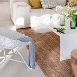 Detalle con butaca de cuerda blanca, botellas verdes sobre mesa blanca, alfombra de yute y taburete de tronco