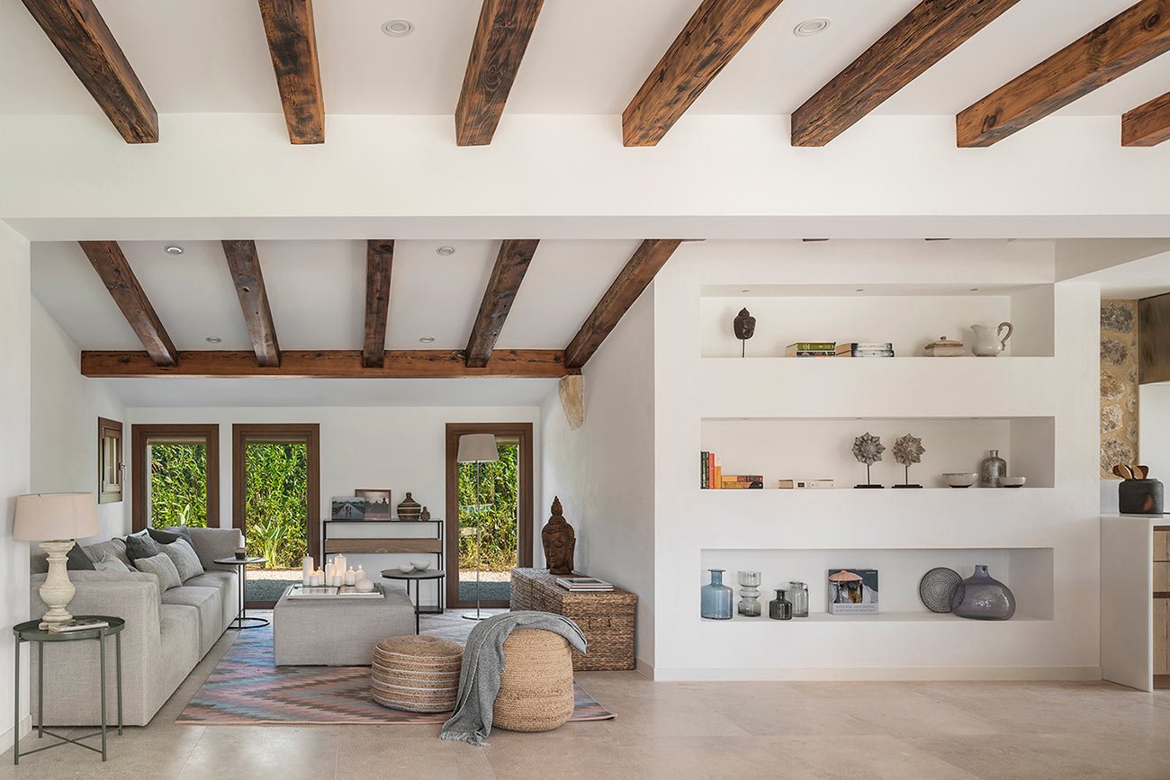 Salón con vigas de madera vistas, sofá gris, estanterías blancas empotradas y suelo beige