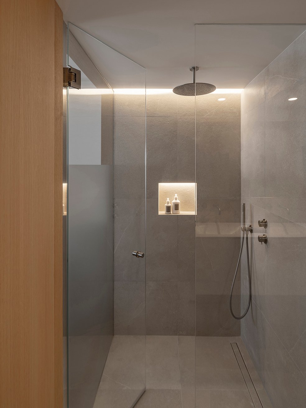 Ducha con mampara de cristal, rociador de techo, hornacina iluminada y revestimiento gris