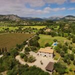 Vista aérea de casa de piedra con tejado de teja, jardines, piscina, viñedo y montañas al fondo