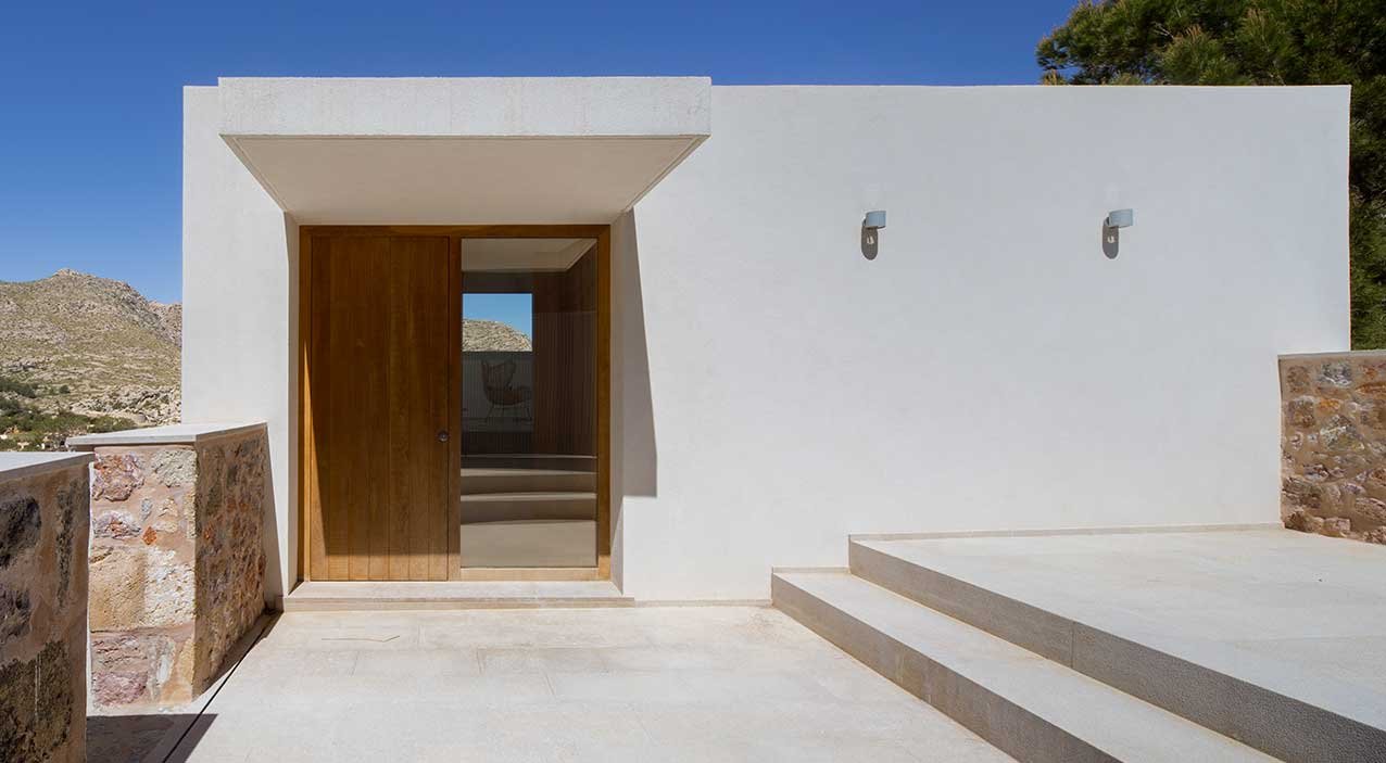 Entrada principal con puerta de madera, muros blancos, muretes de piedra y escalones de piedra clara