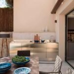Mesa con cuencos de cerámica azul en primer plano y cocina exterior de acero inoxidable al fondo