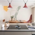 Isla de cocina con placa de cocción y comedor al fondo con mural de formas geométricas de colores