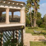 Esquina de la casa con terraza cubierta, pérgola de madera, persianas azules y hamaca sobre el césped