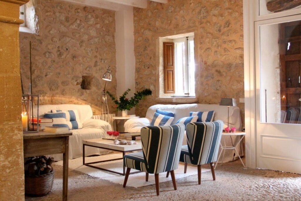 Salón de Can Suau Vell con muros de piedra, sofás blancos y sillones de rayas azules