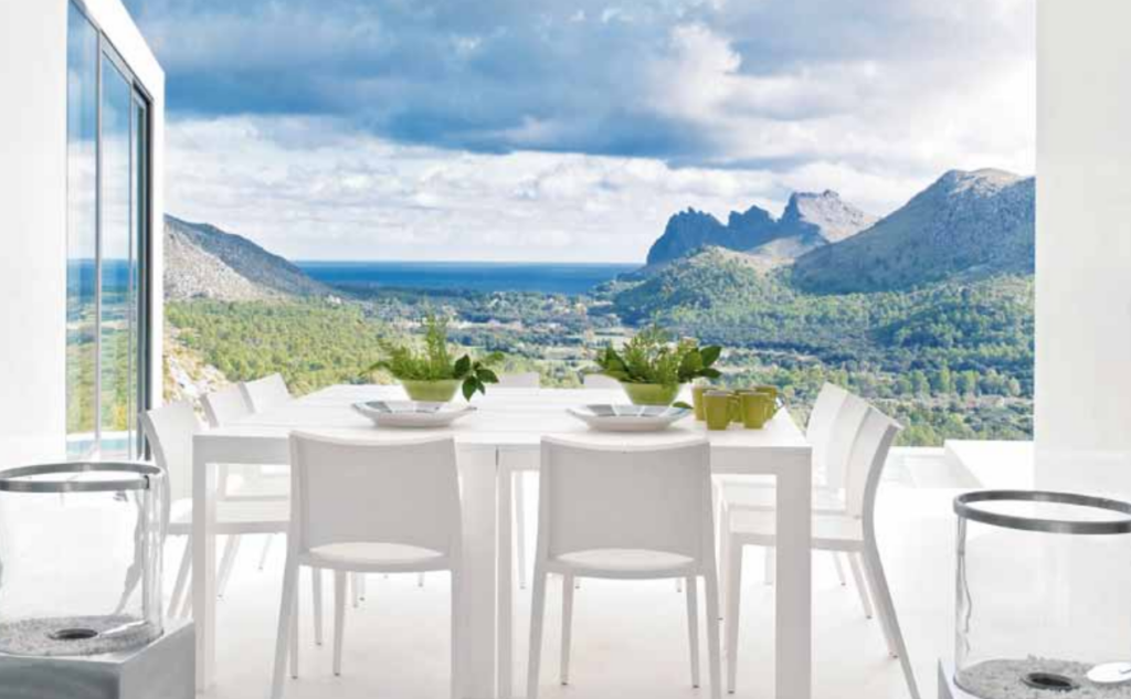 Terraza luminosa de LF115 con mesa y sillas blancas, cuencos verdes y vistas a montañas y mar
