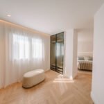 Vestidor con armarios de cristal y marco negro, puf ovalado, visillos y vista al dormitorio