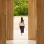 Puertas de roble abiertas hacia una escalinata de piedra clara, con una persona de espaldas y jardín