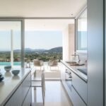 Cocina abierta a la terraza, isla con encimera veteada y vistas a la piscina y al valle