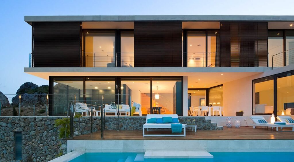 Fachada de la casa LF115 al anochecer con lamas de madera, piscina y terraza iluminada