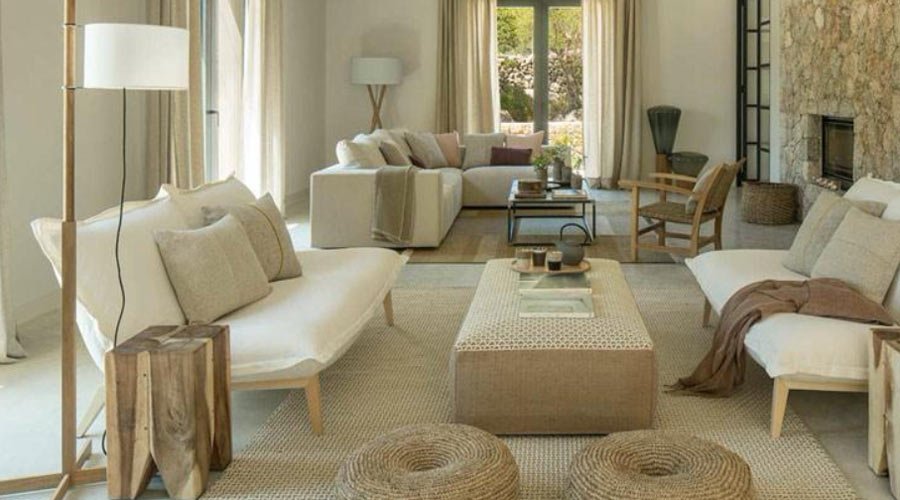 Salón de LF323 con sofás en tonos crudos, alfombra de yute, pufs de cuerda y chimenea de piedra