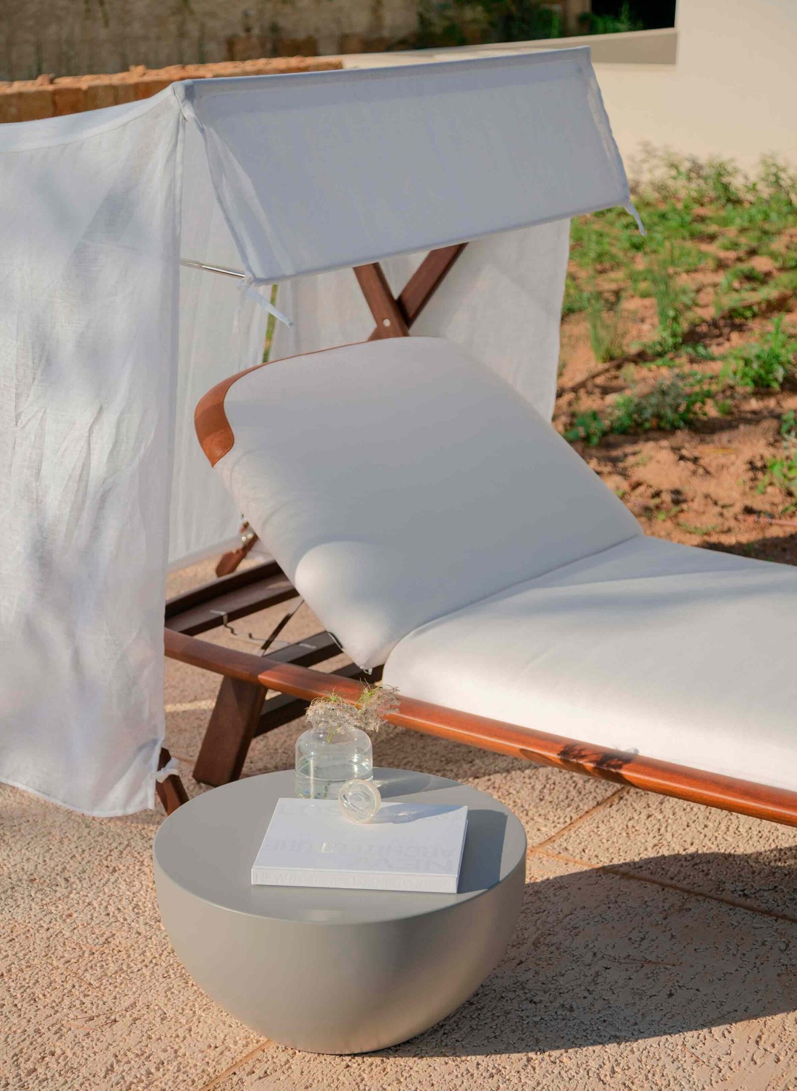 Tumbona de madera con cojín blanco y tela de lino, mesa auxiliar gris y suelo de terraza