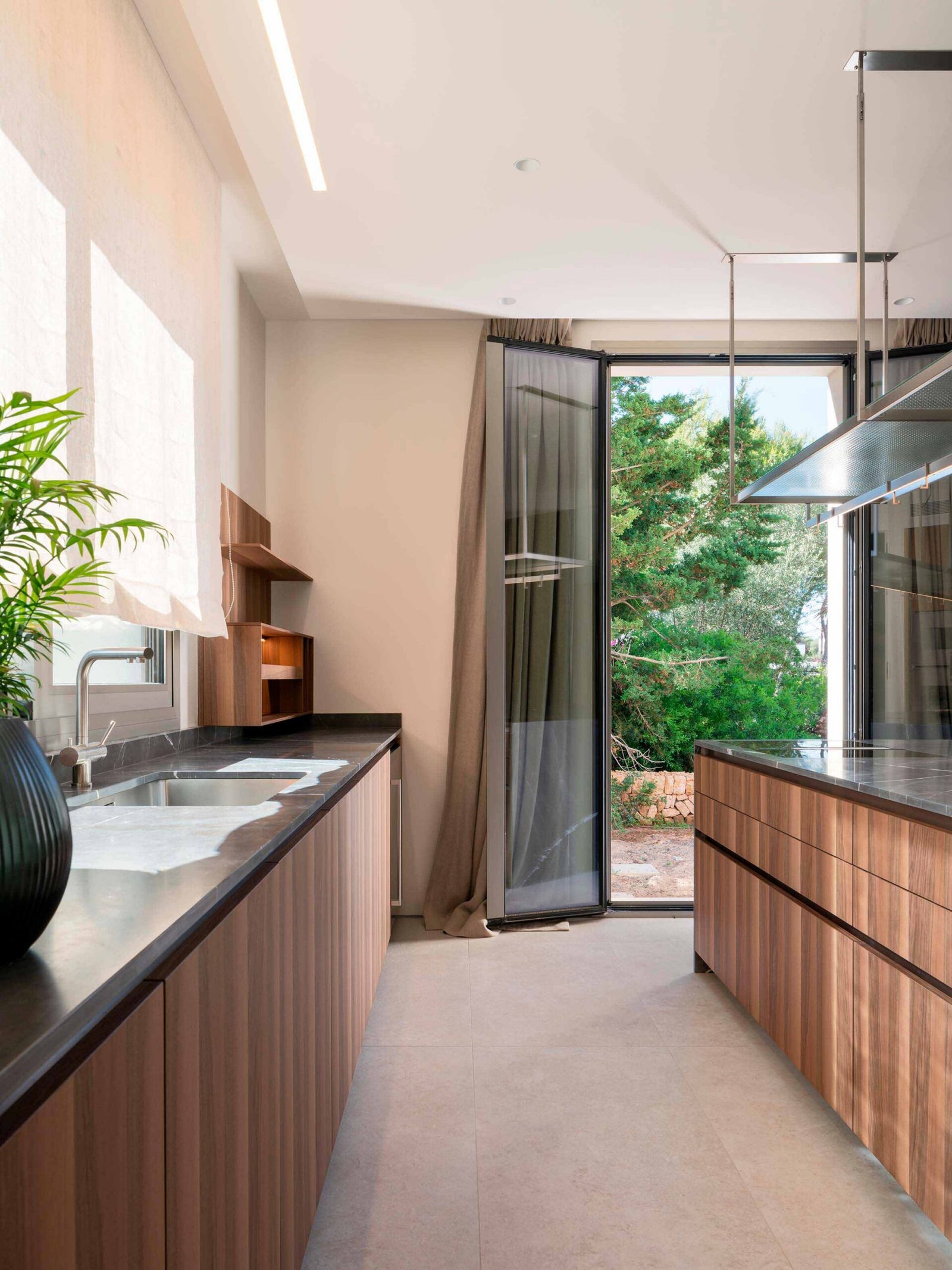 Cocina con encimera oscura, muebles de madera, fregadero y puerta acristalada abierta al jardín
