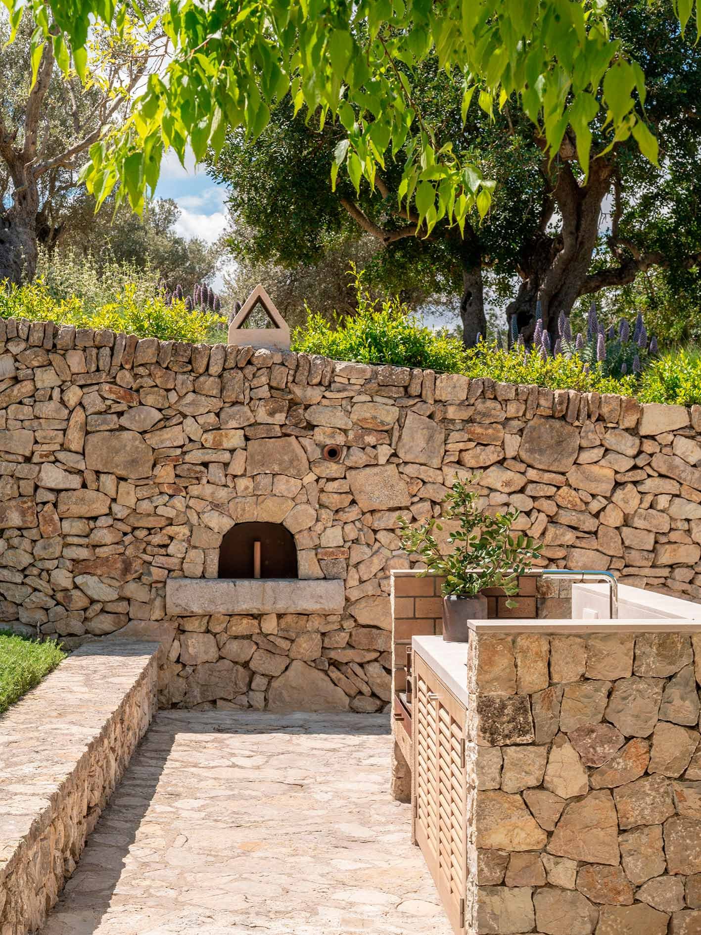 Rincón de cocina exterior con horno de leña empotrado en un muro de piedra seca