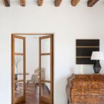 Detalle de vigas de madera vistas, puertas acristaladas de madera y cómoda antigua con lámpara