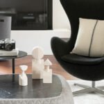 Detalle de butaca negra con cojín claro, mesa baja con esculturas blancas y cámara de fotos analógica