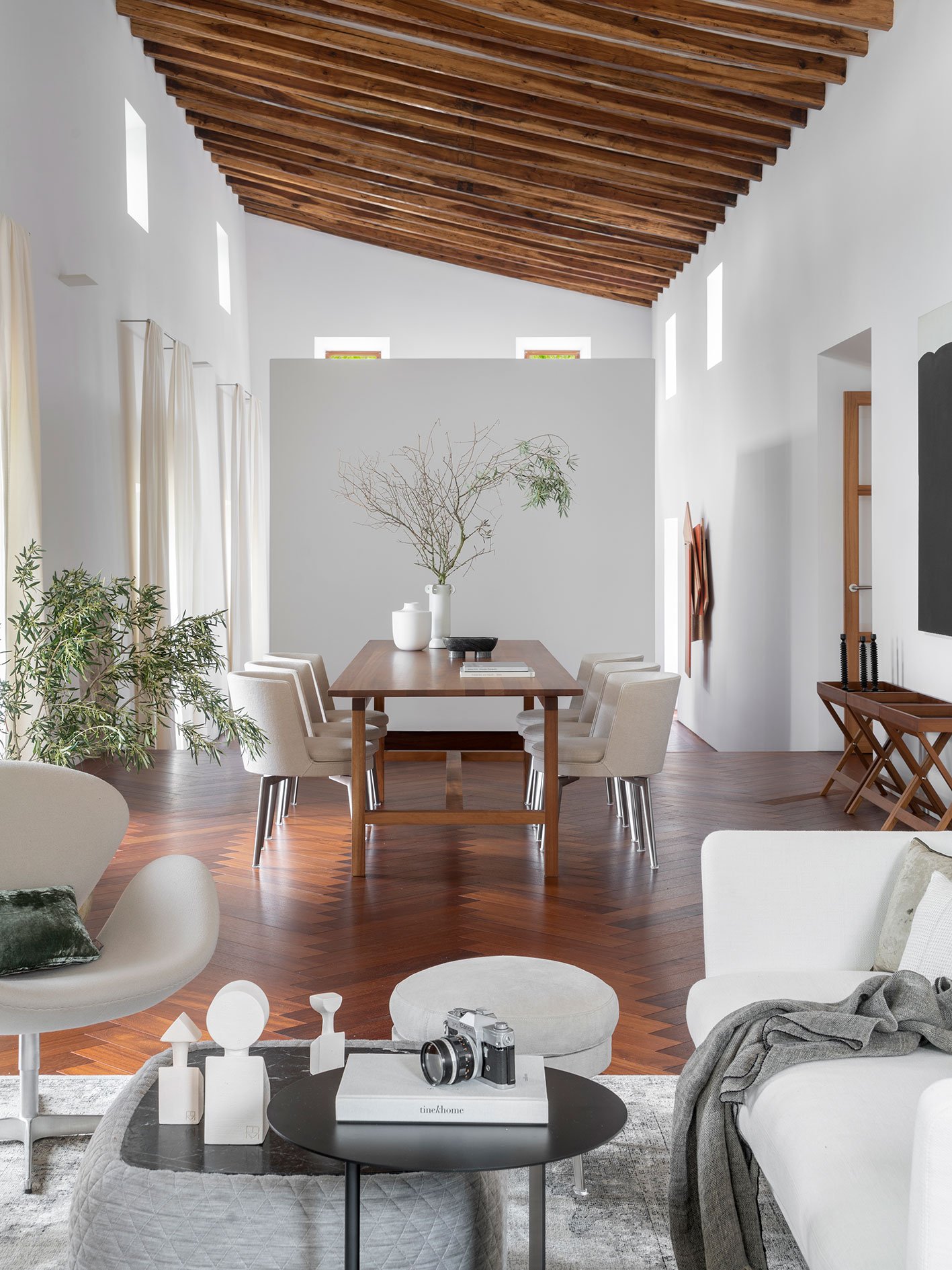 Comedor de techo inclinado con vigas de madera, mesa larga, sillas tapizadas y suelo en espiga