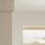 Detalle de moldura clásica de escayola con relieve floral en una columna blanca y luz suave al fondo