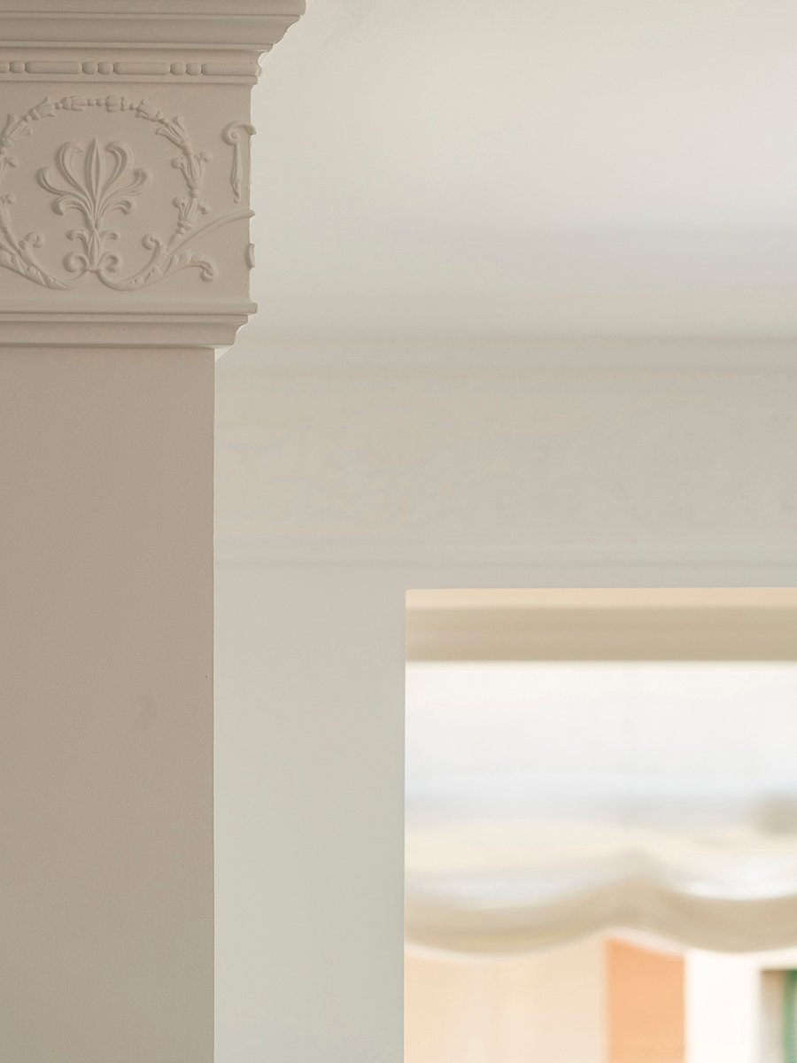 Detalle de moldura clásica de escayola con relieve floral en una columna blanca y luz suave al fondo