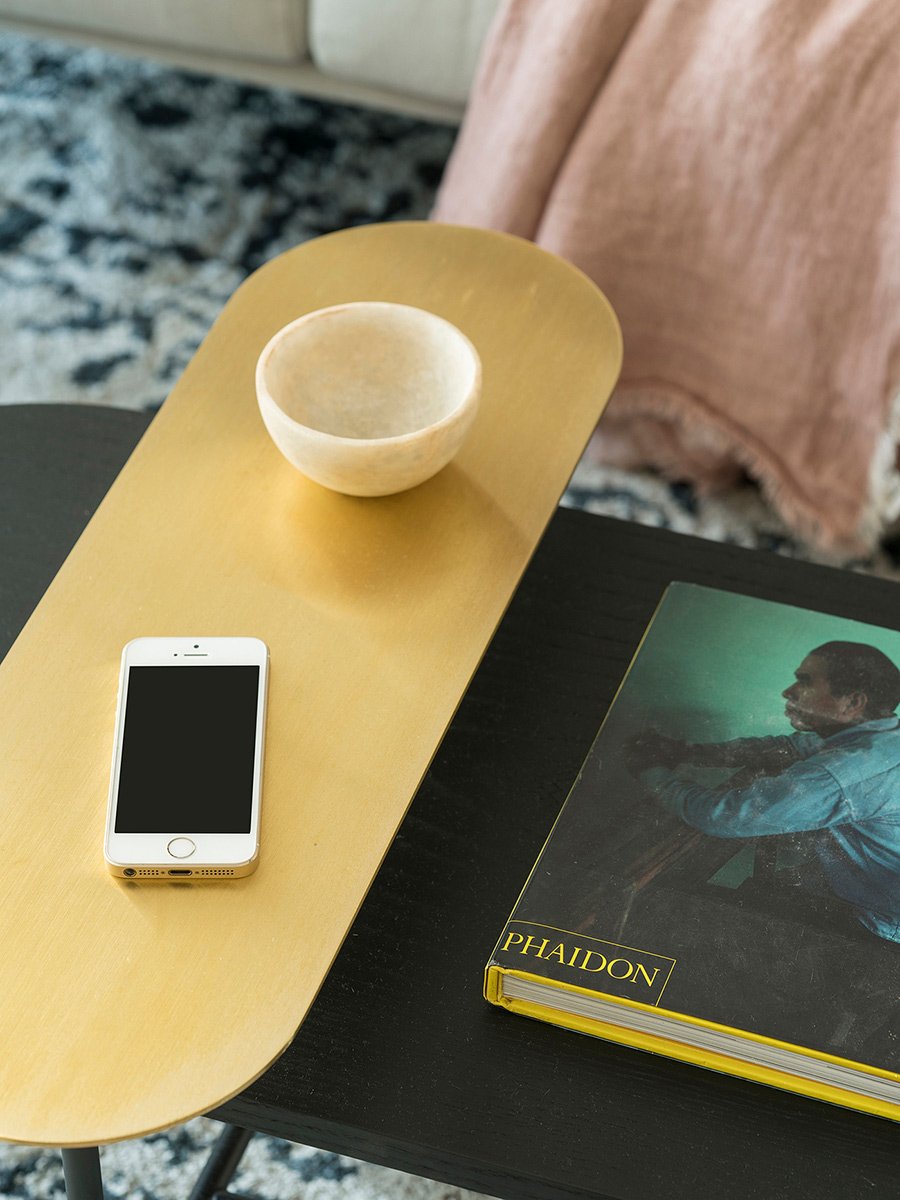 Detalle de mesa de centro con tablero de latón dorado, cuenco de piedra clara y libro de arte