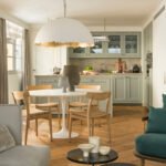 Comedor con mesa redonda blanca y sillas de roble con asiento trenzado, cocina verde al fondo
