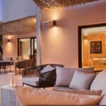 Zona de estar exterior con sofá trenzado y cojines bajo toldo, comedor al aire libre y jardín