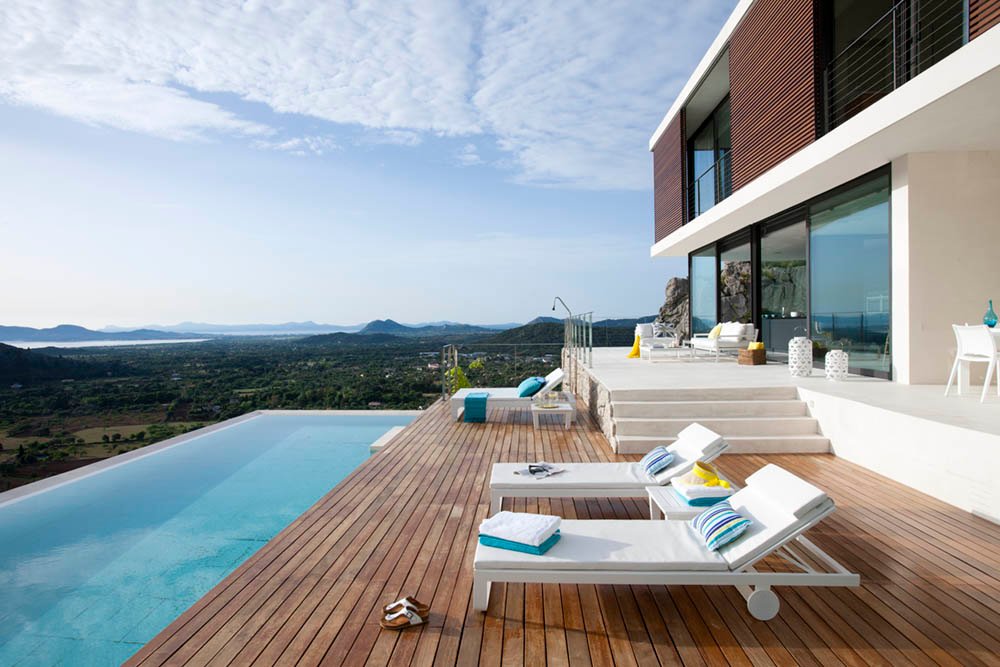 Vista desde la tarima de madera a lo largo de la piscina, con tumbonas y horizonte de montañas