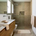 Baño con ducha a ras de suelo revestida en piedra beige, mueble de madera y lavabo blanco