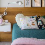Cama infantil con cabecero de madera, ropa de cama verde, colcha rosa, cojines estampados y lámpara articulada
