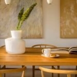 Detalle de la mesa de madera con jarrón blanco, planta verde, taza, libro abierto y lámparas colgantes