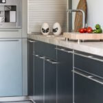 Detalle de puertas de cocina con tiradores metálicos, encimera de piedra y tomates sobre tabla de madera.