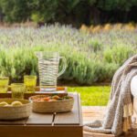 Detalle de mesa de madera con jarra de cristal, vasos verdes, cestas de fruta y manta estampada