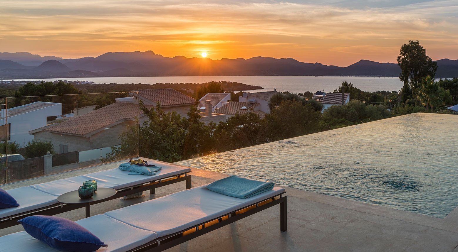 Atardecer sobre el mar y las montañas desde la terraza, con tumbonas y piscina infinita
