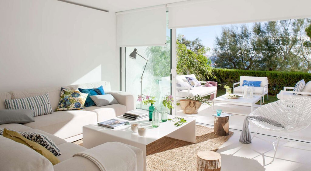 Salón luminoso con sofá crema, mesa blanca y alfombra de yute, abierto a terraza y jardín