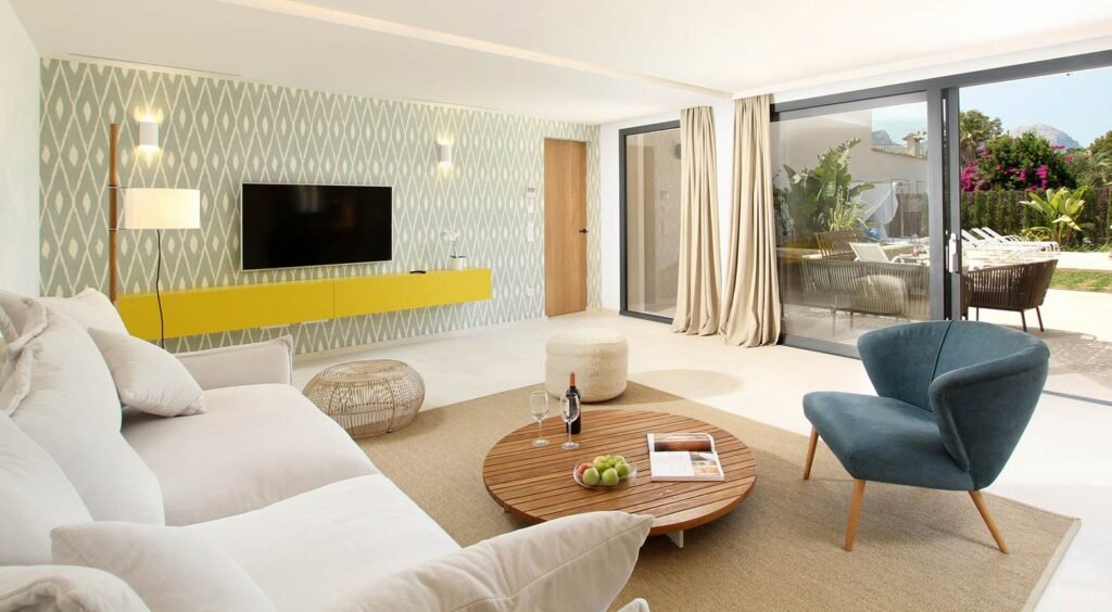 Salón con sofá blanco, sillón azul, mesa baja redonda de madera y mueble amarillo bajo la televisión