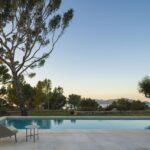 Piscina al atardecer con pino, muro de piedra seca y vistas al mar y a la montaña