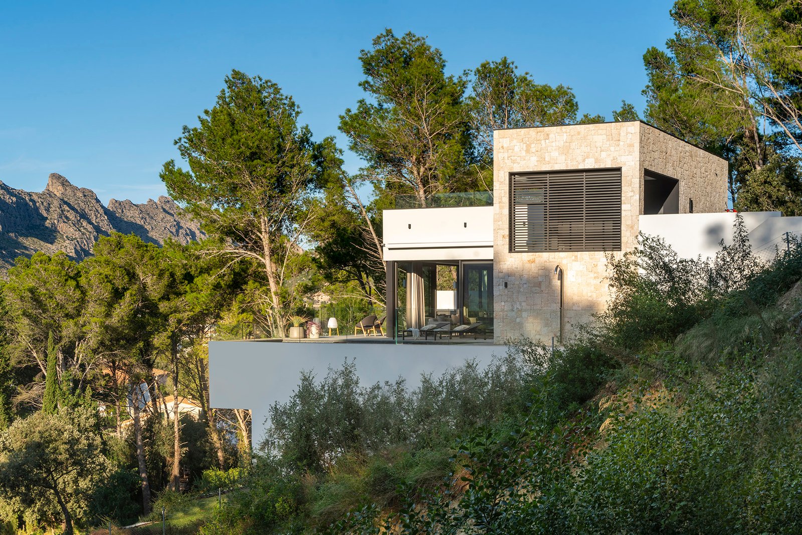 Villa G137 de piedra natural y blanco integrada en el pinar con la sierra al fondo